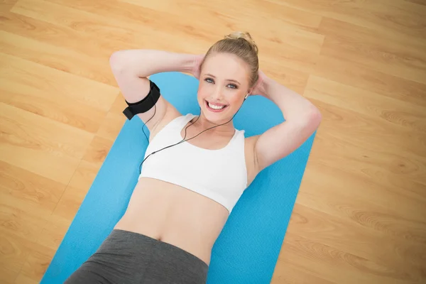 Smiling sporty blonde listening to music and exercising — Stock Photo, Image