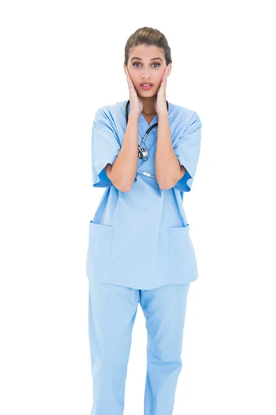 Enfermeira surpreendida em esfoliação azul posando com a cabeça nas mãos — Fotografia de Stock