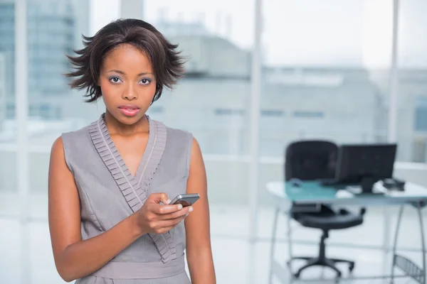 Mujer de negocios no sonriente de pie en su oficina y mensajes de texto — Foto de Stock