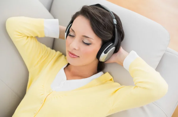 Relaxed casual brunette in yellow cardigan listening to music with headphones — Stock Photo, Image