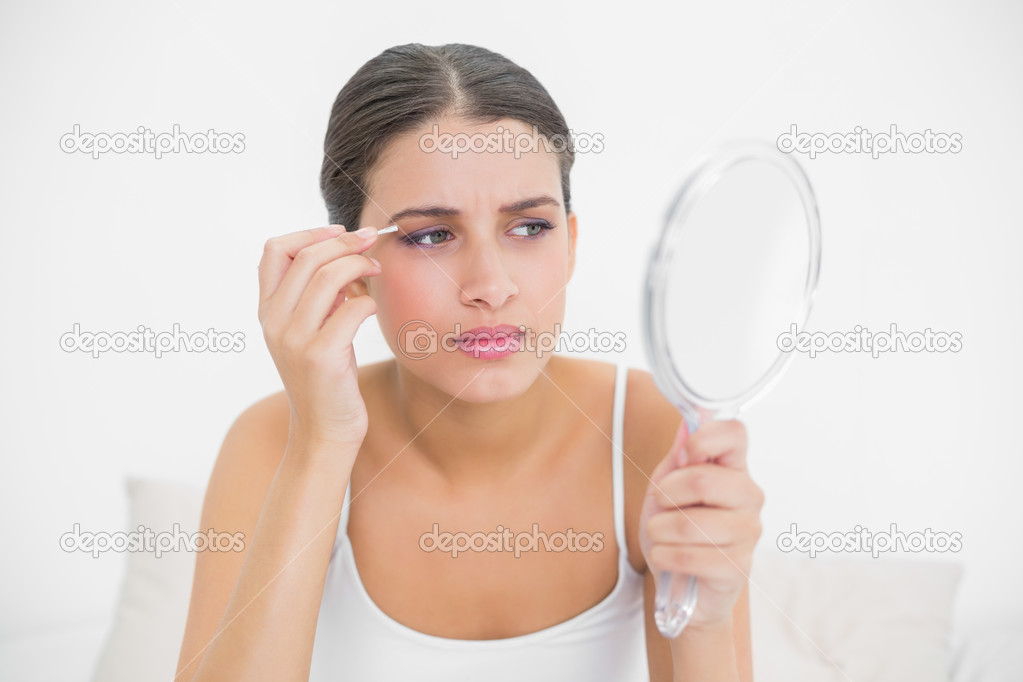 Model in white pajamas plucking her eyebrows