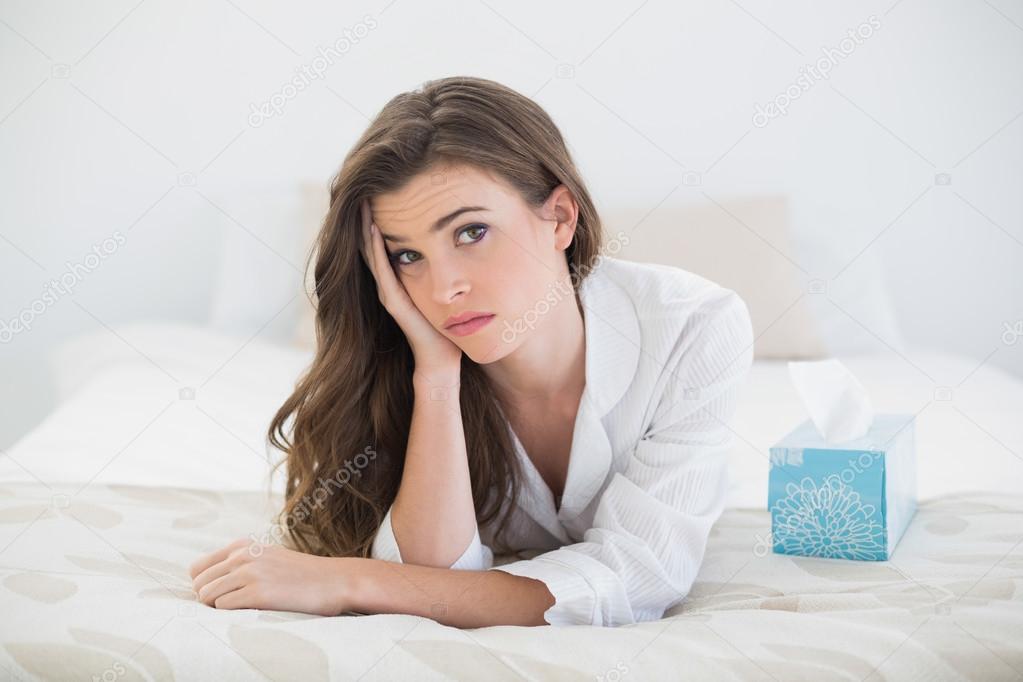 Worried woman in white pajamas lying on her bed
