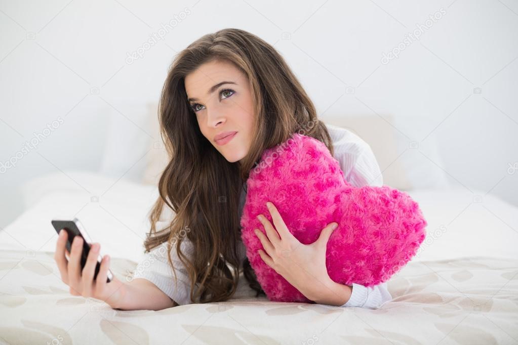 Woman holding a mobile phone and a heart-shaped pillow