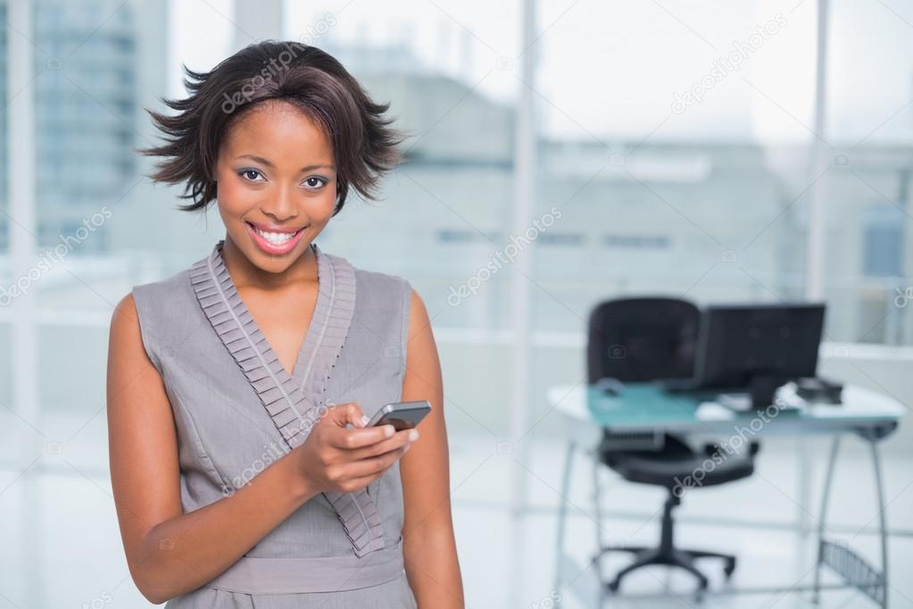 Smiling woman standing in her office and using her phone