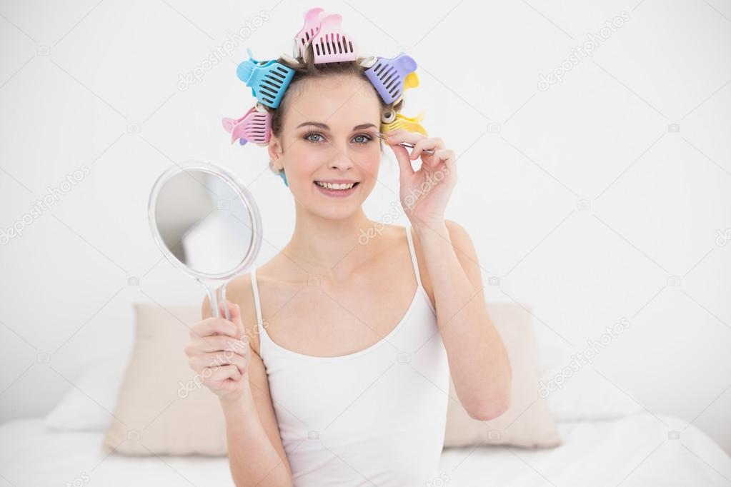 Amused woman in hair curlers plucking her eyebrows