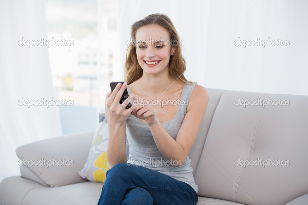 Happy young woman sitting on couch using smartphone