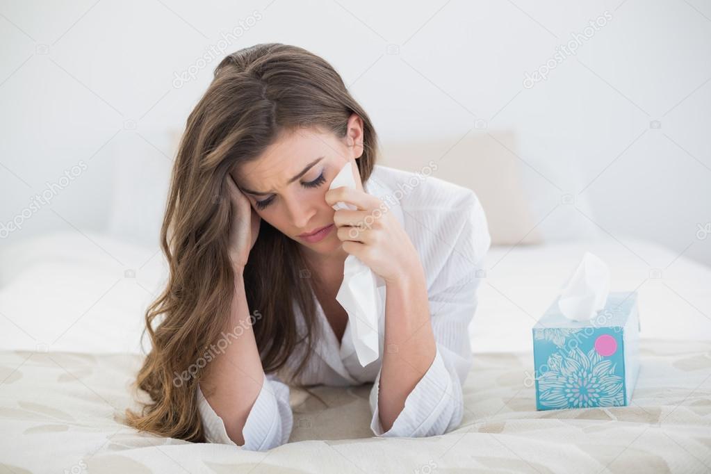 Depressed woman in white pajamas crying on her bed