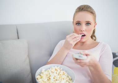 casual stupito bionda tenendo il telecomando e mangiare popcornsarışın uzak tutarak ve patlamış mısır yemek Casual hayret