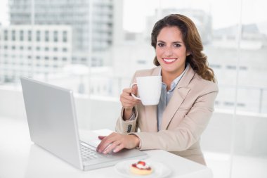 dizüstü bilgisayar masasında kullanarak ve kupa holding iş kadını gülümseyen