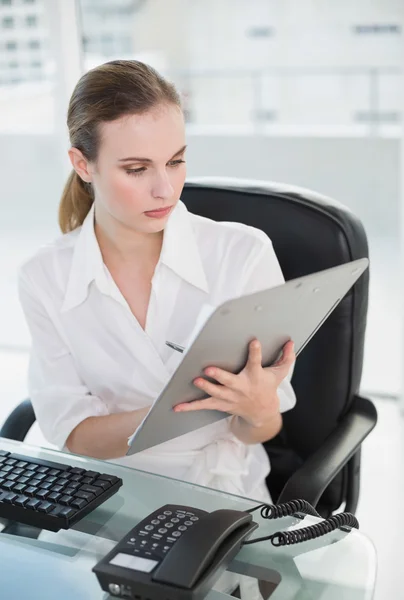 Mujer de negocios seria escribiendo en el portapapeles sentado en el escritorio — Foto de Stock