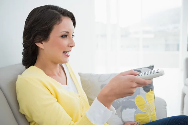 Peaceful casual brunette in yellow cardigan changing tv channel — Stock Photo, Image