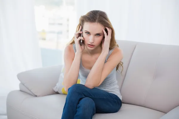 Stressed young woman sitting on couch talking on smartphone — Stock Photo, Image