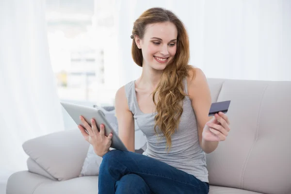 Pretty young woman sitting on couch using tablet — Stock Photo, Image