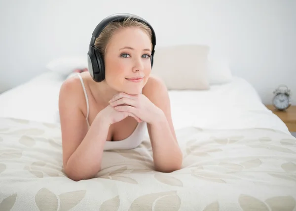 Natürlich lächelnde Blondine, die auf dem Bett liegt und Musik hört — Stockfoto