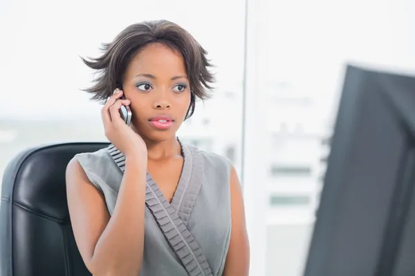 Серйозна жінка розмовляє по телефону, дивлячись на екран комп'ютера — стокове фото