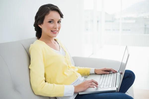 Charming casual brunette in yellow cardigan using a laptop — Stock Photo, Image