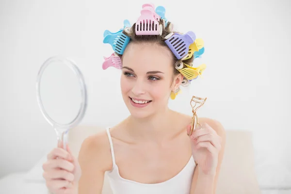 Mulher bonita em encrespadores de cabelo olhando-se em um espelho — Fotografia de Stock