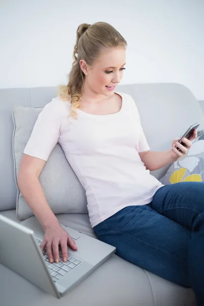 Свободно улыбающаяся блондинка с помощью смартфона и ноутбука — стоковое фото