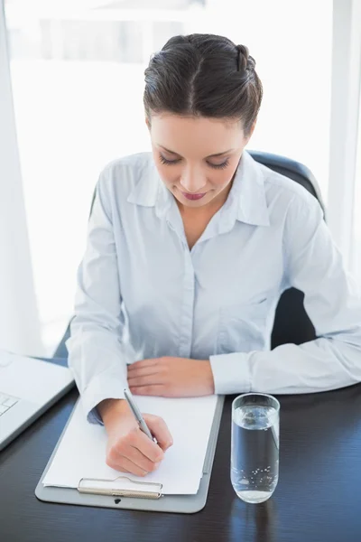 Concentrated stylish brunette businesswoman taking notes on a clipboard — Stock Photo, Image
