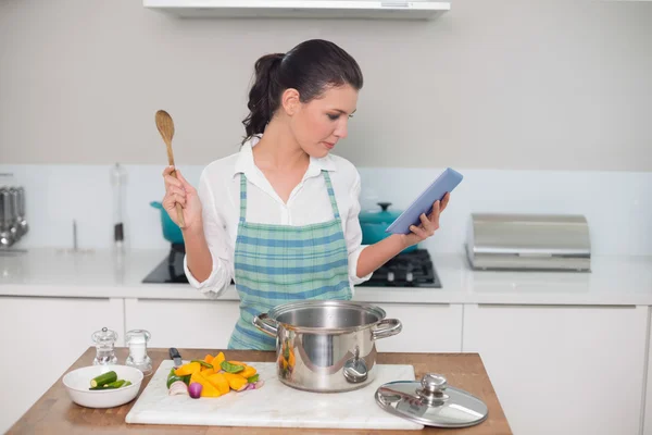 Yemek yaparken tablet kullanarak önlük giyen kadın — Stok fotoğraf