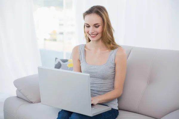 Joyeux jeune femme assise sur le canapé en utilisant un ordinateur portable — Photo