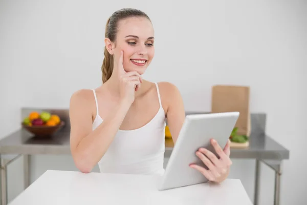 Pensant jeune femme heureuse en utilisant sa tablette à la table — Photo