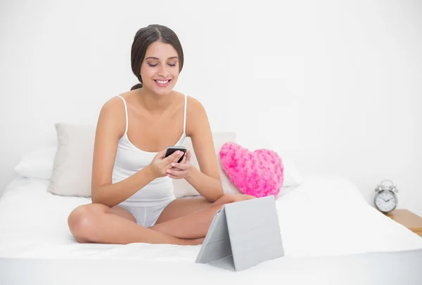 Modell im weißen Pyjama beim SMS-Schreiben mit einem Mobiltelefon — Stockfoto