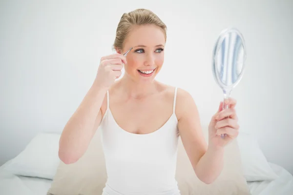 Natürliche fröhliche Blondine hält Spiegel und benutzt Pinzette — Stockfoto