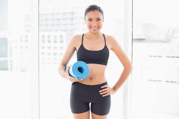 Modelo sonriente en ropa deportiva que lleva una alfombra de ejercicio azul — Foto de Stock