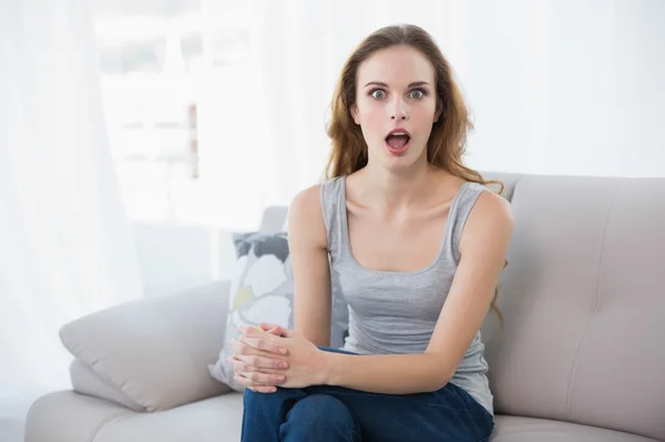 Shocked young woman sitting on couch — Stock Photo, Image