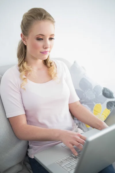 Lässig schöne Blondine sitzt auf der Couch mit Laptop — Stockfoto