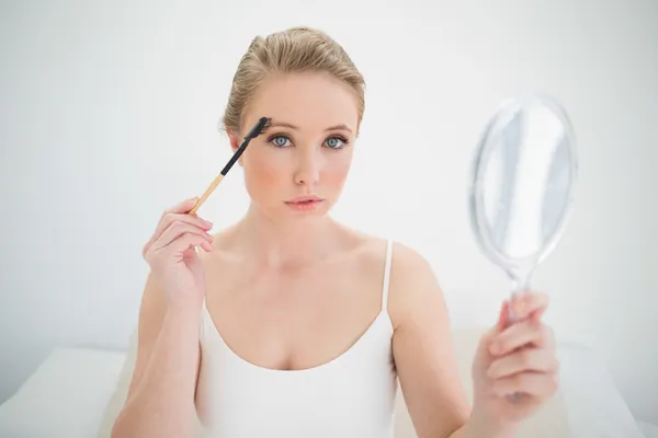 Rubia popa natural sosteniendo espejo y usando cepillo de cejas — Foto de Stock