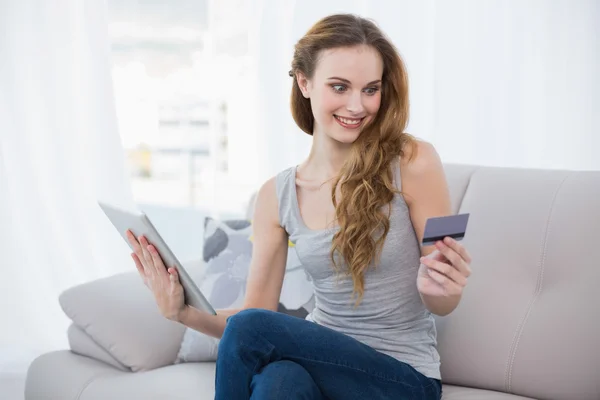 Cheerful young woman sitting on couch using tablet for shopping online — Stock Photo, Image