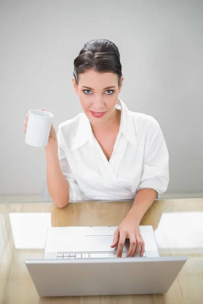 Fredliga affärskvinna arbetar på bärbar dator håller kaffe — Stockfoto