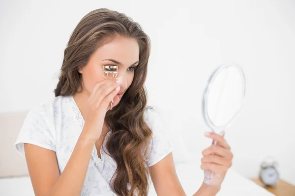 Brunette using an eyelash curler and mirror — Stock Photo, Image