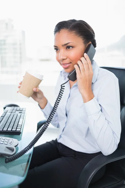 Thinking young businesswoman answering the telephone while holding a cup of coffee — Stock Photo, Image