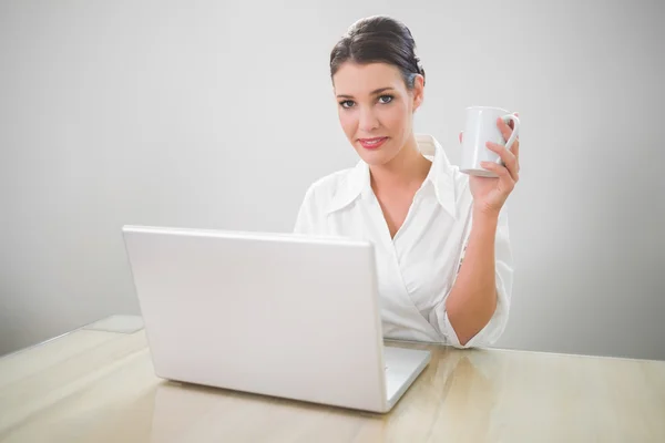 Cheerful businesswoman working on laptop holding coffee — Stock Photo, Image