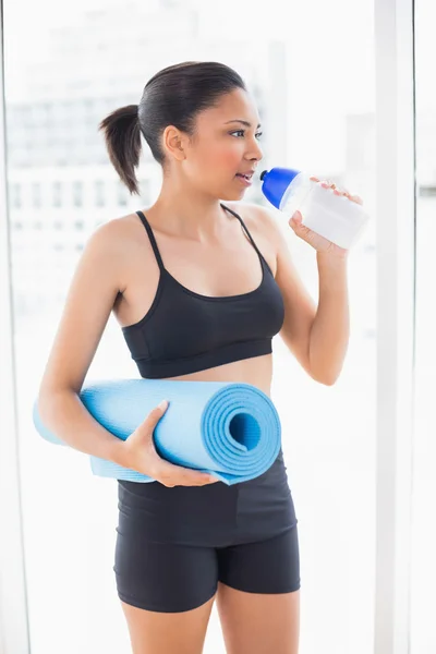Серьезная модель в спортивной одежде с ковриком для упражнений и питьевой водой — стоковое фото