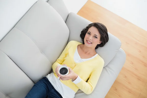 Zufriedene lässige Brünette in gelber Strickjacke mit einer Tasse Kaffee — Stockfoto