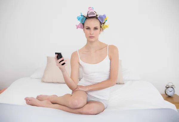 Frowning woman in hair curlers holding a mobile phone — Stock Photo, Image