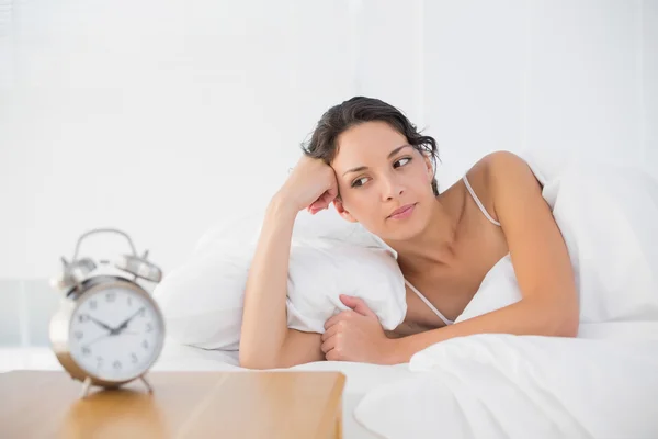 Thoughtful casual brunette in white pajamas lying in her bed — Stock Photo, Image