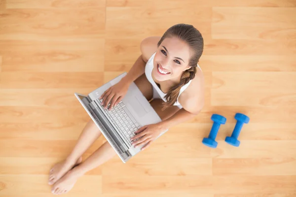 Lachende sportieve brunette met behulp van een laptop — Stockfoto