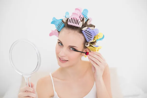 Beautiful woman in hair curlers applying mascara — Stock Photo, Image