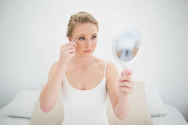 Natural serious blonde holding mirror and using tweezers — Stock Photo, Image