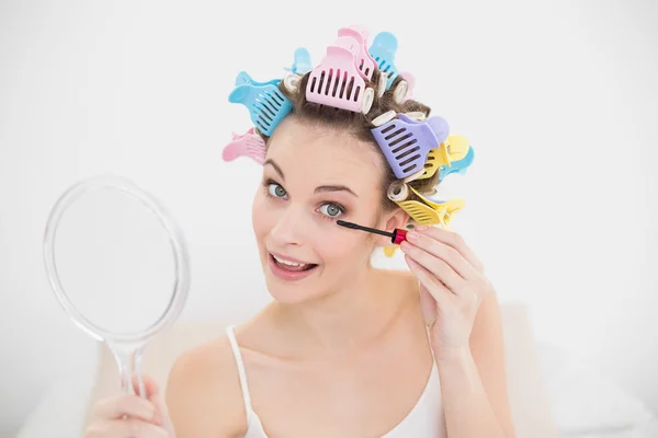 Cheerful woman in hair curlers applying mascara — Stock Photo, Image