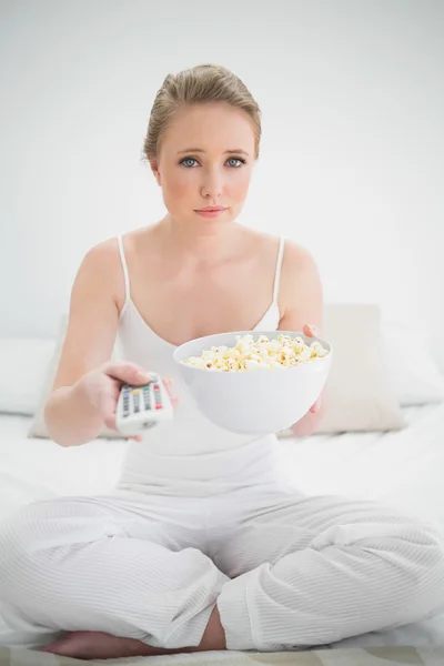 Natural stern blonde holding remote and popcorn — Stock Photo, Image