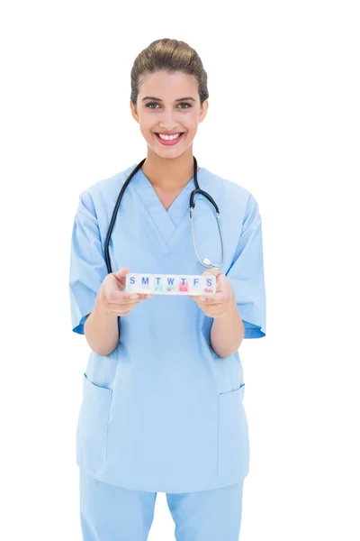 Enfermeira feliz em azul esfrega segurando uma caixa de medicação — Fotografia de Stock