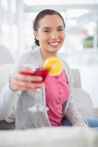 Mujer sonriente sentada en el sofá y mostrando cóctel — Foto de Stock