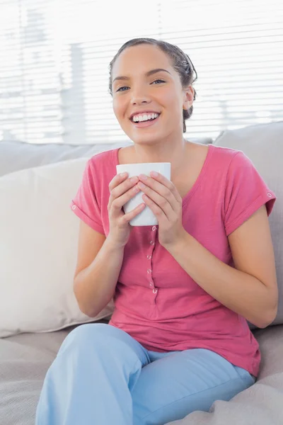 Lachende vrouw zitten op bank holding mok van koffie — Stockfoto