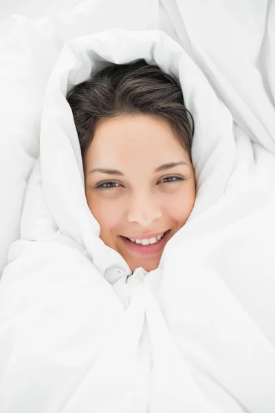 Lächelnde lässige Brünette eingewickelt in ihre Bettdecke — Stockfoto
